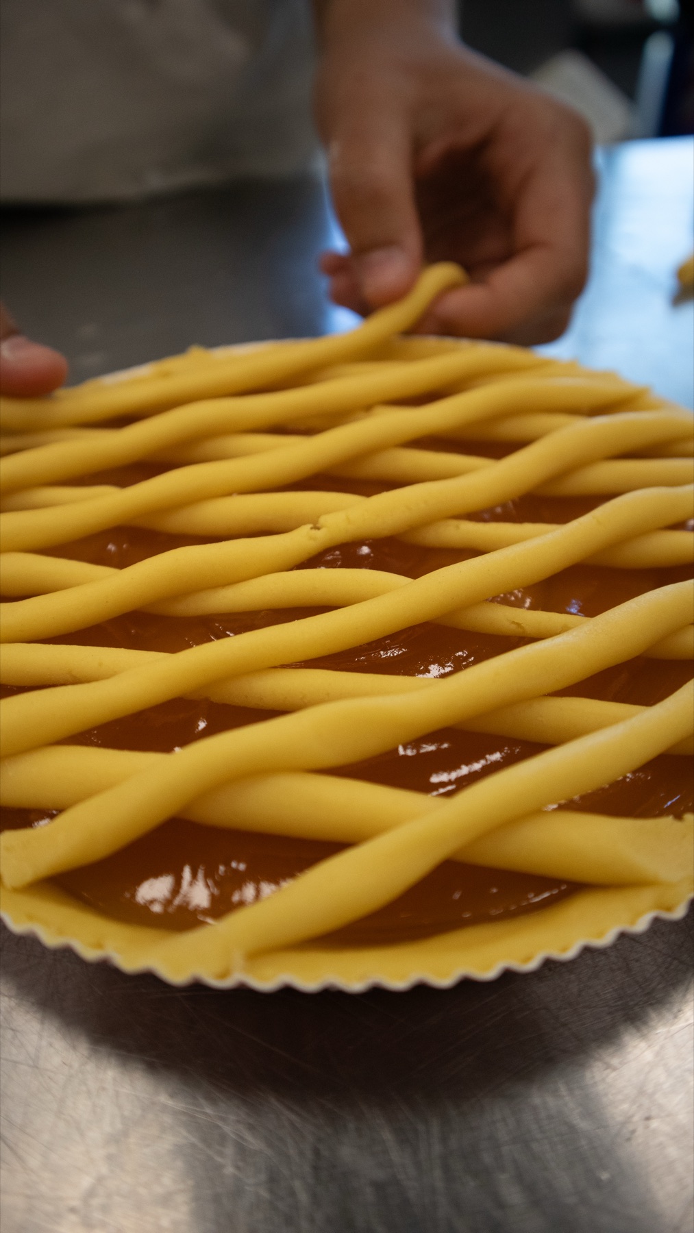 Le mani di una pasticcera che intrecciano la griglia di frolla su una crostata
